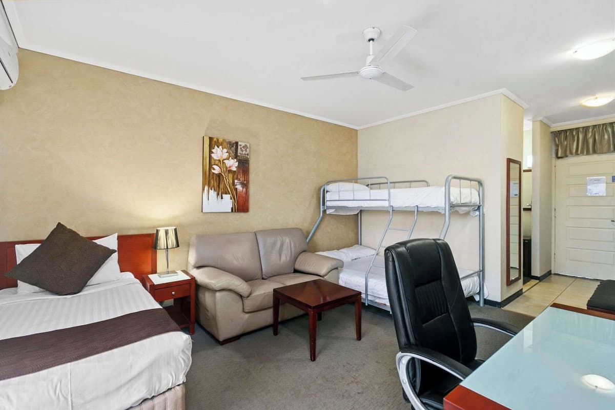 Ein Hotelzimmer mit Bett, Sofa, Schreibtisch, Stuhl, Stockbett und einem Wandbild.