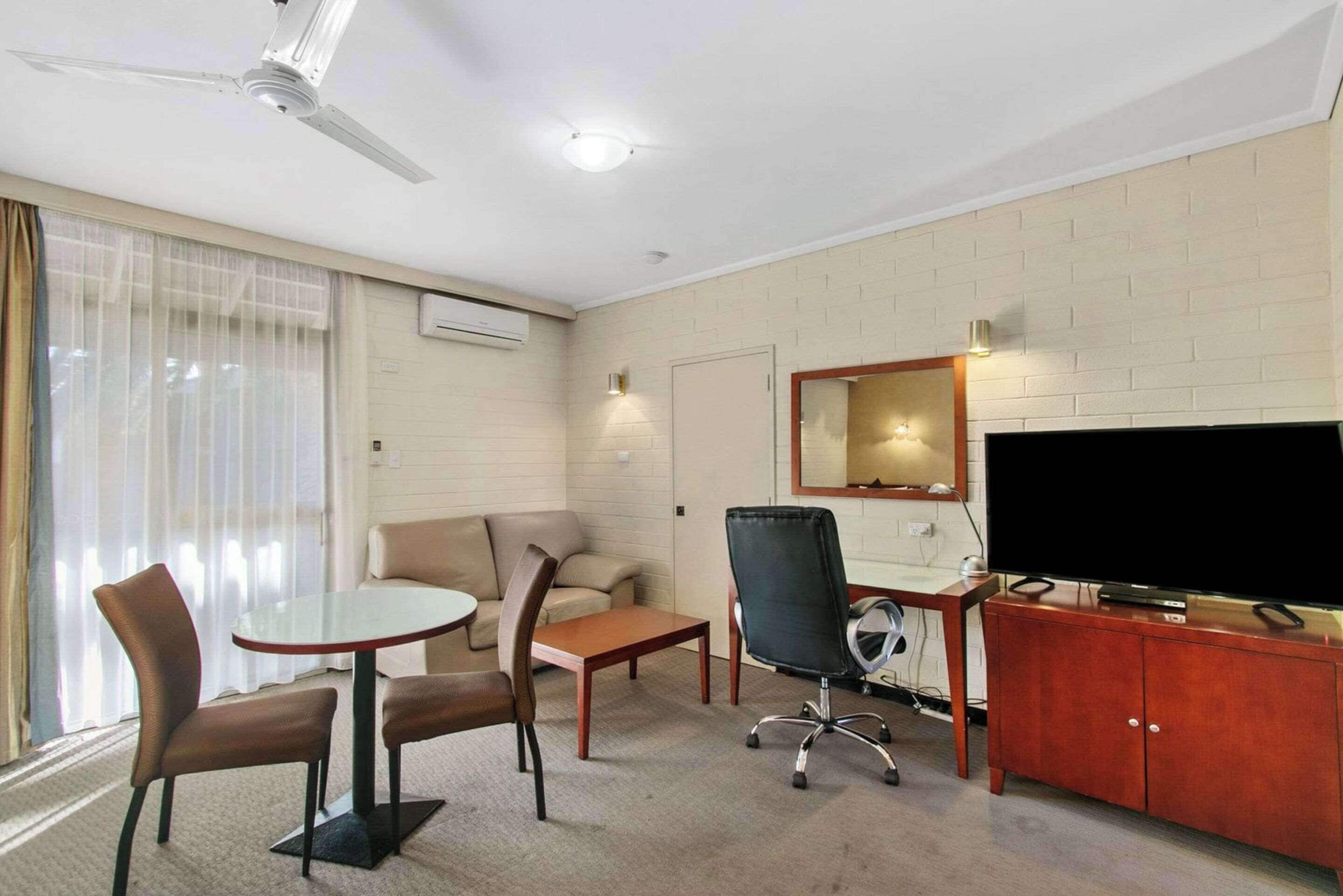 A hotel room with a flat-screen TV, a sofa, a coffee table, and a dining table with chairs.