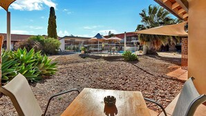 An outdoor patio area with a table and chairs, surrounded by a pergola, palm trees, and a view of a building with a red roof. - Comfort Inn Whyalla (Whyalla Playford)