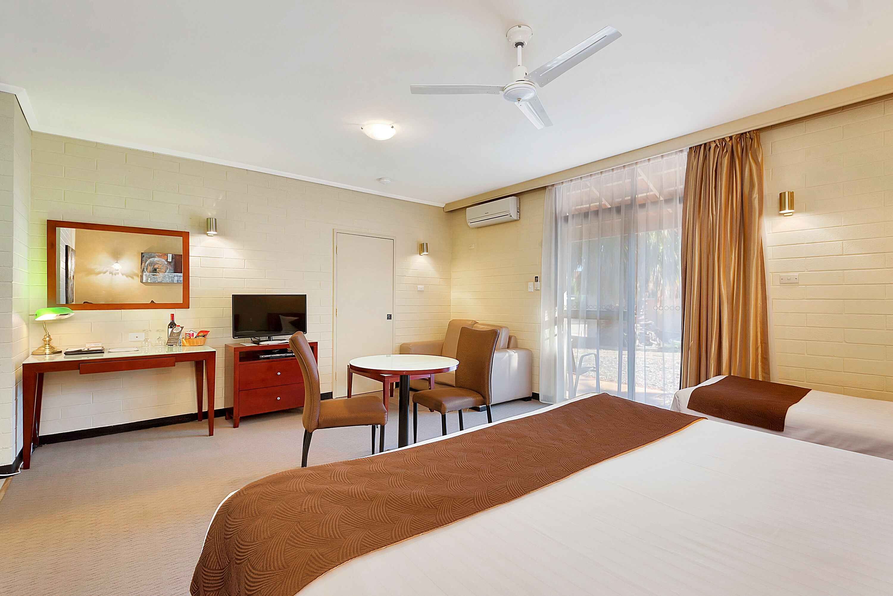 Habitación de hotel con cama, escritorio con televisor, silla, mesita y ventana con cortinas.