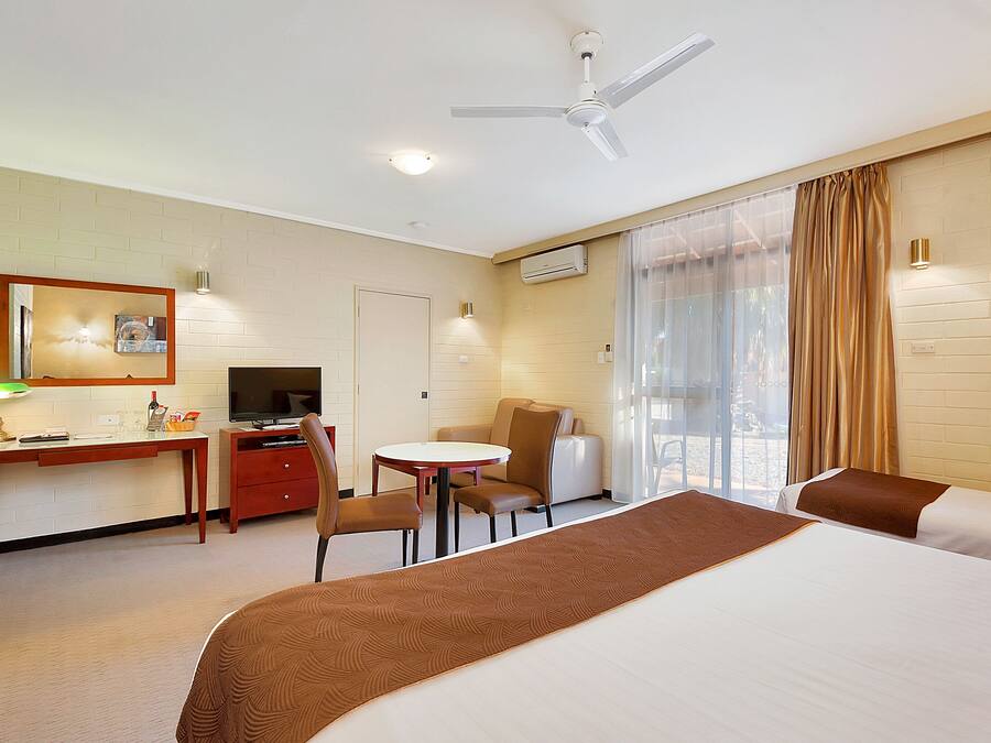 A hotel room with a bed, a desk with a TV, a chair, a small table, and a window with curtains.