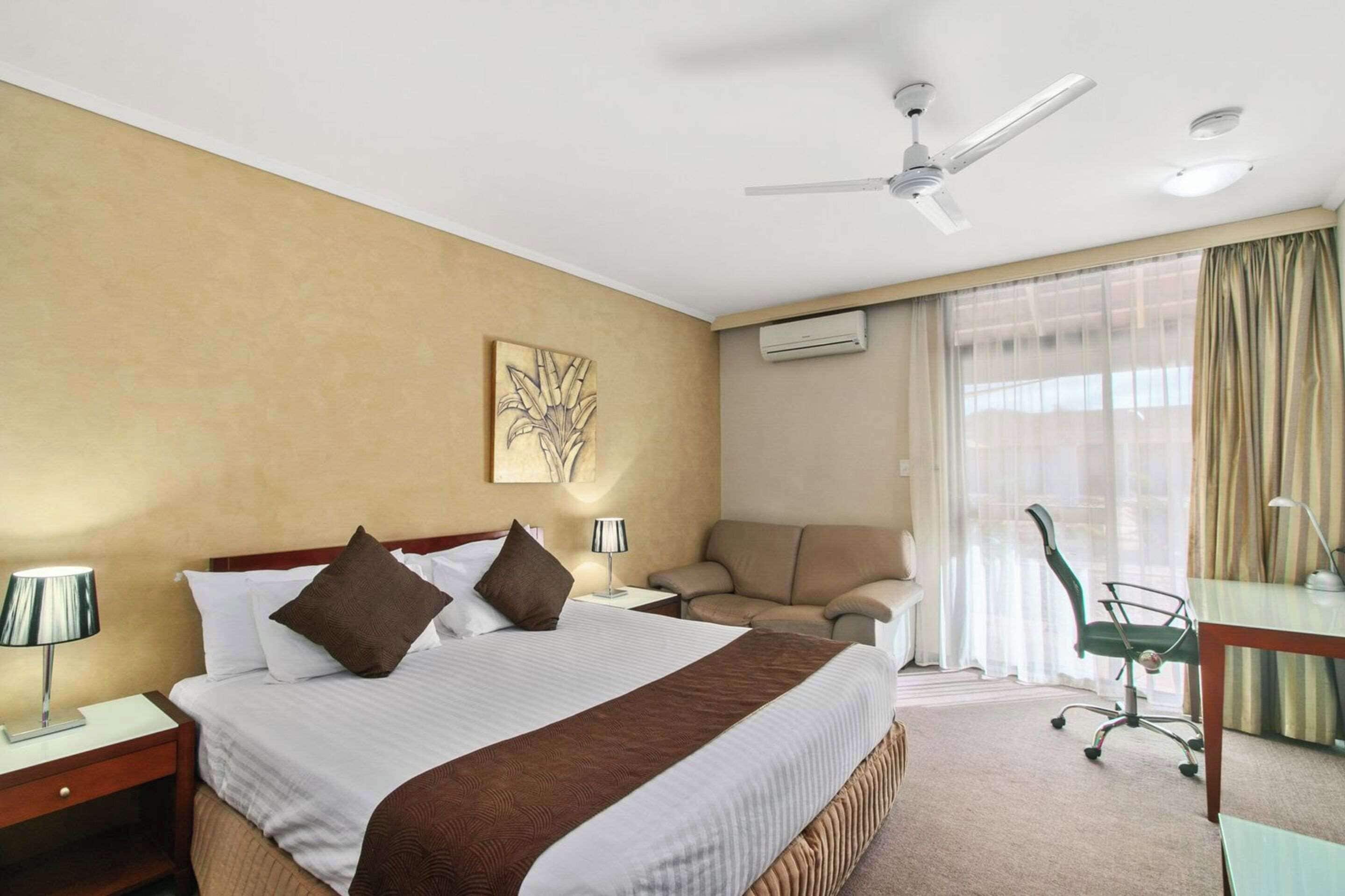 Una habitación de hotel con una cama grande, un escritorio, una silla y un ventilador de techo.