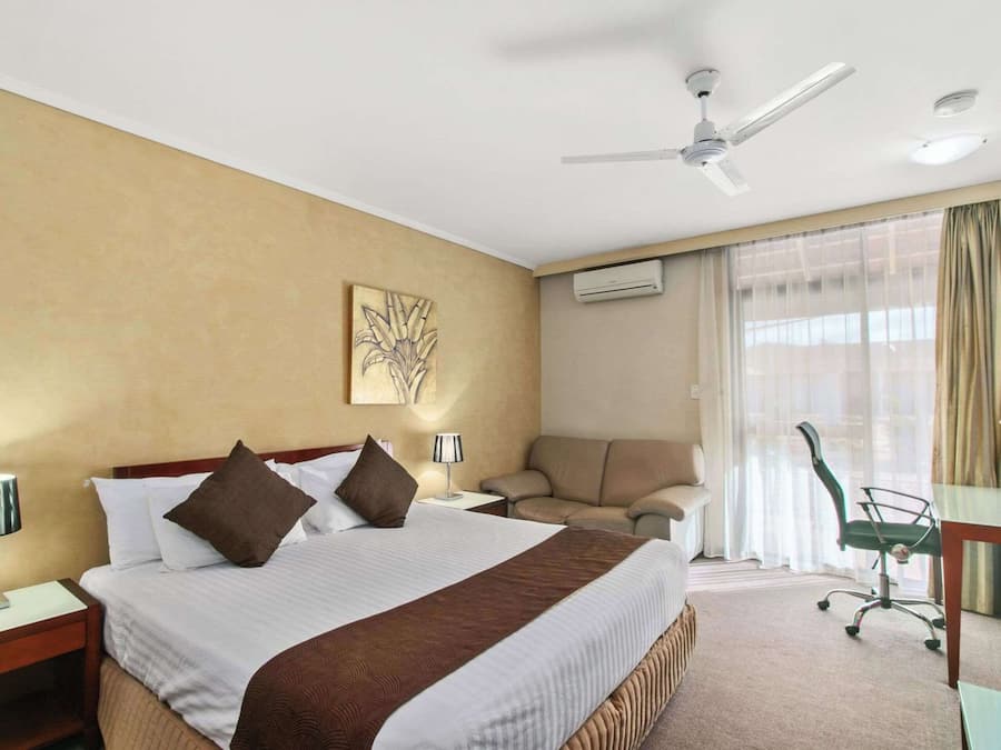 Una habitación de hotel con una cama grande, un escritorio, una silla y un ventilador de techo.