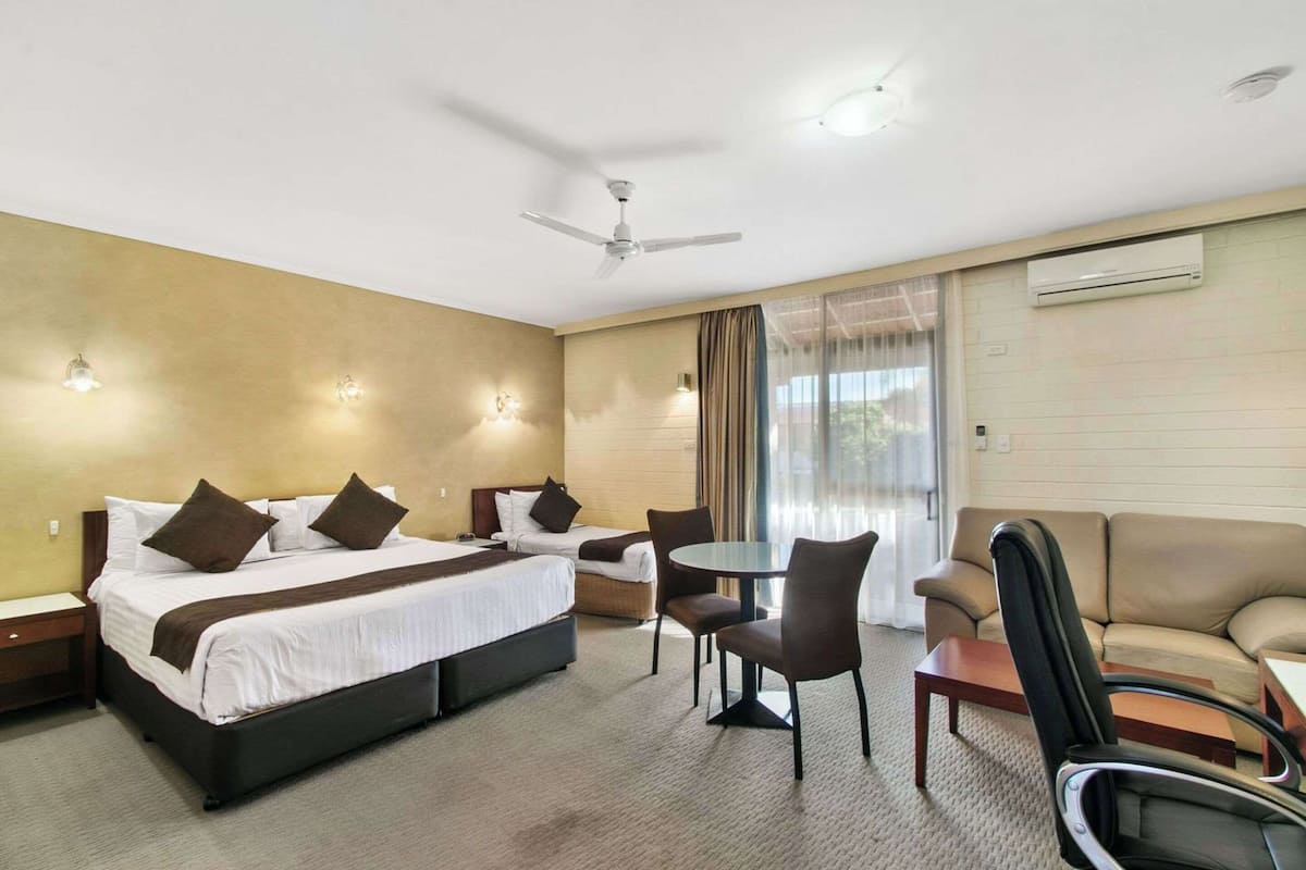 Ein Hotelzimmer mit einem Bett, zwei Sesseln, einem kleinen Tisch, einer Couch, einem Deckenventilator und einer Klimaanlage.