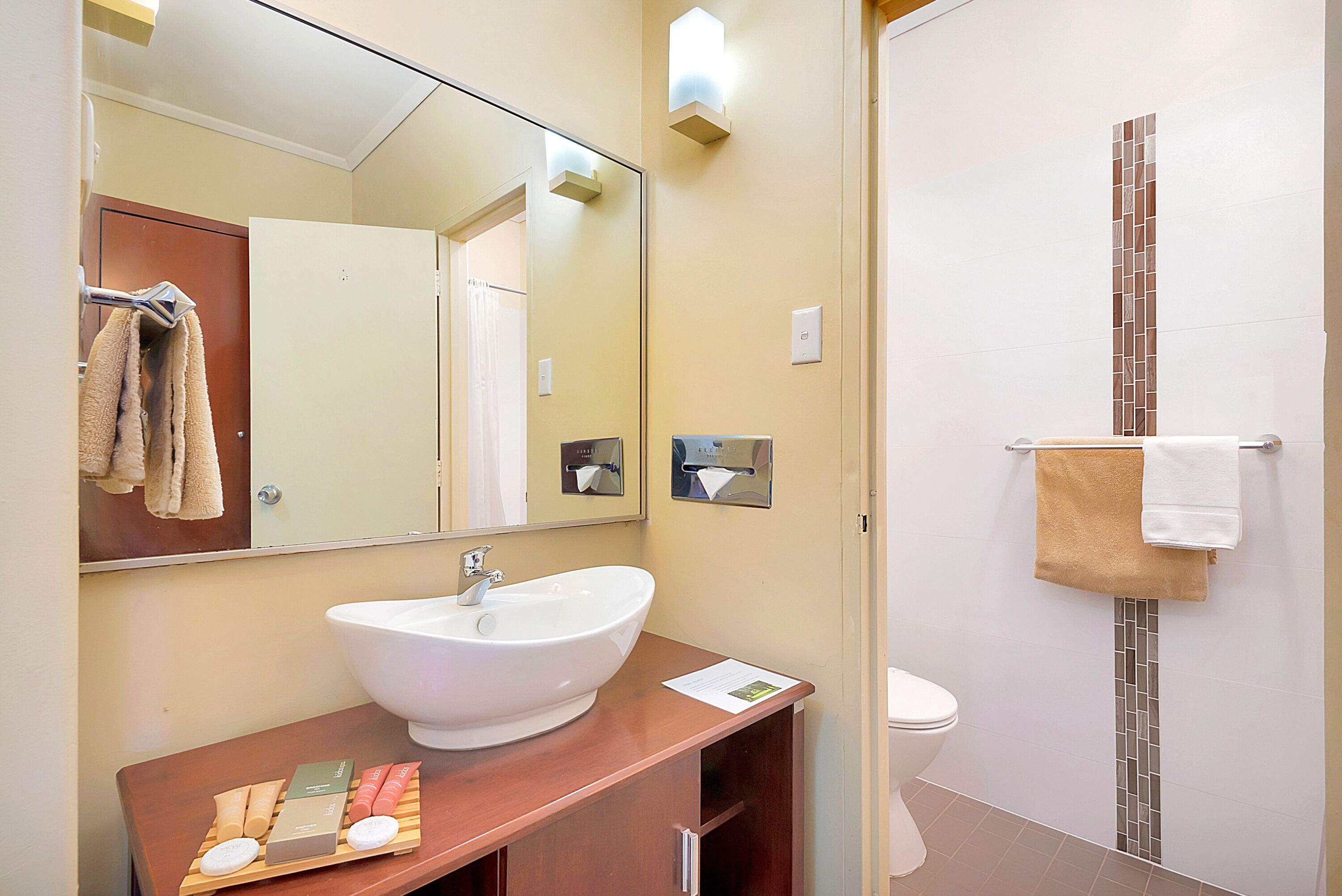Un baño con lavamanos blanco, espejo y toallero.