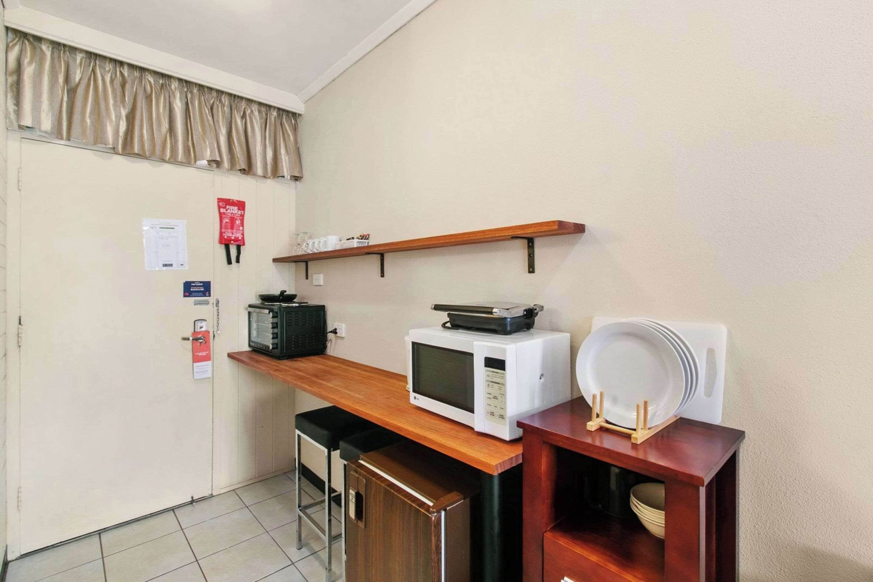 A compact kitchenette with a microwave, toaster, and a small shelf above the counter.