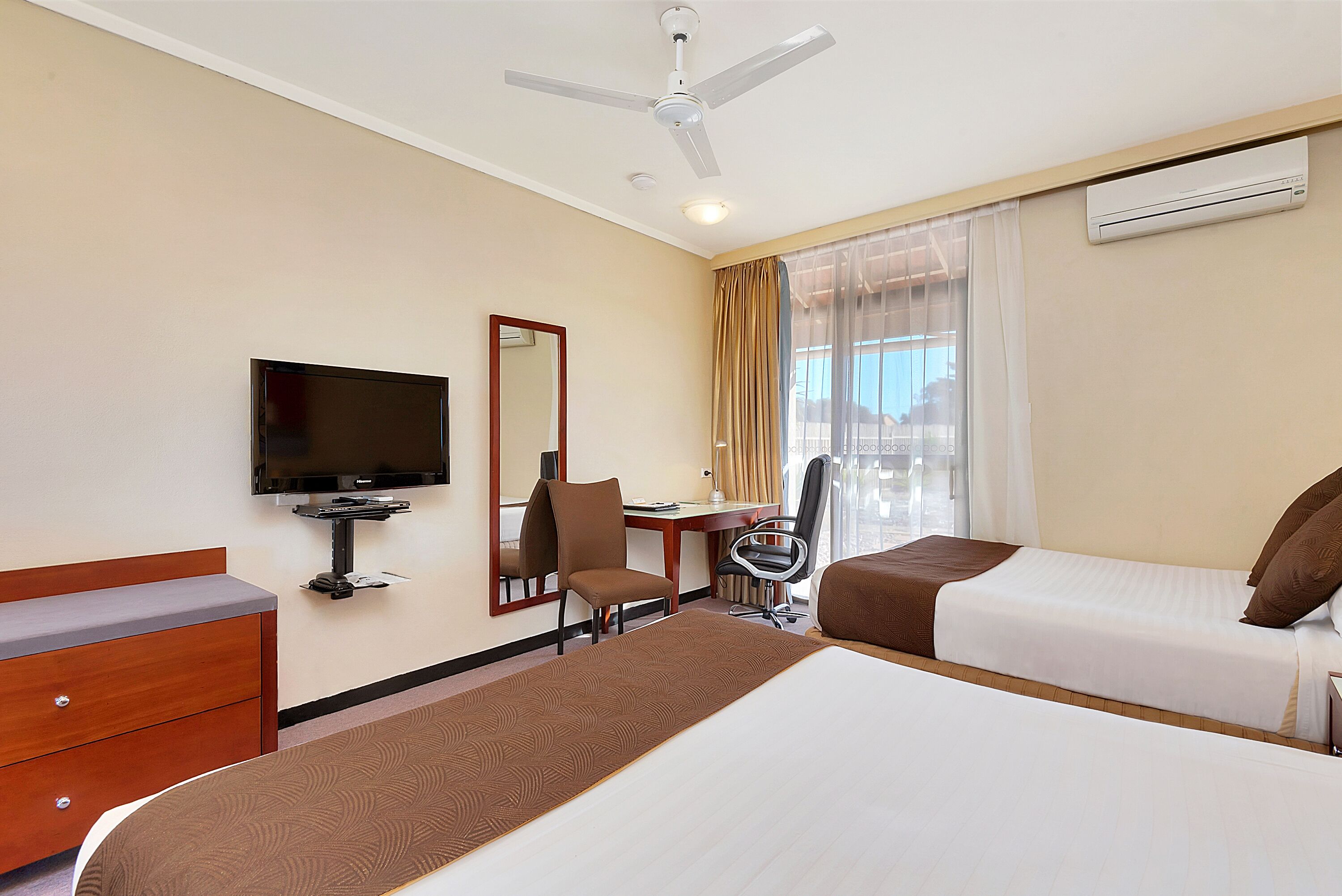 A hotel room with a bed, a desk, a chair, a television, and an air conditioning unit.