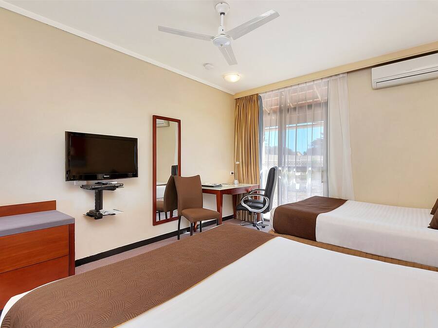 A hotel room with a bed, a desk, a chair, a television, and an air conditioning unit.