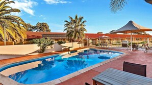 A swimming pool with lounge chairs and umbrellas, surrounded by palm trees and a building with a red roof. - Comfort Inn Whyalla (Whyalla Playford)