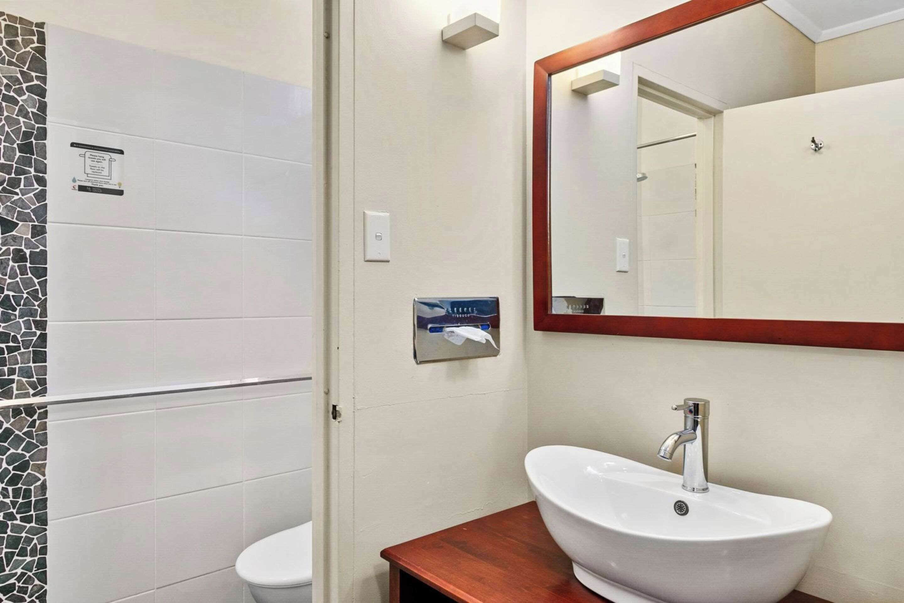 A bathroom with a white toilet, a sink with a wooden countertop, and a mirror with a wooden frame.