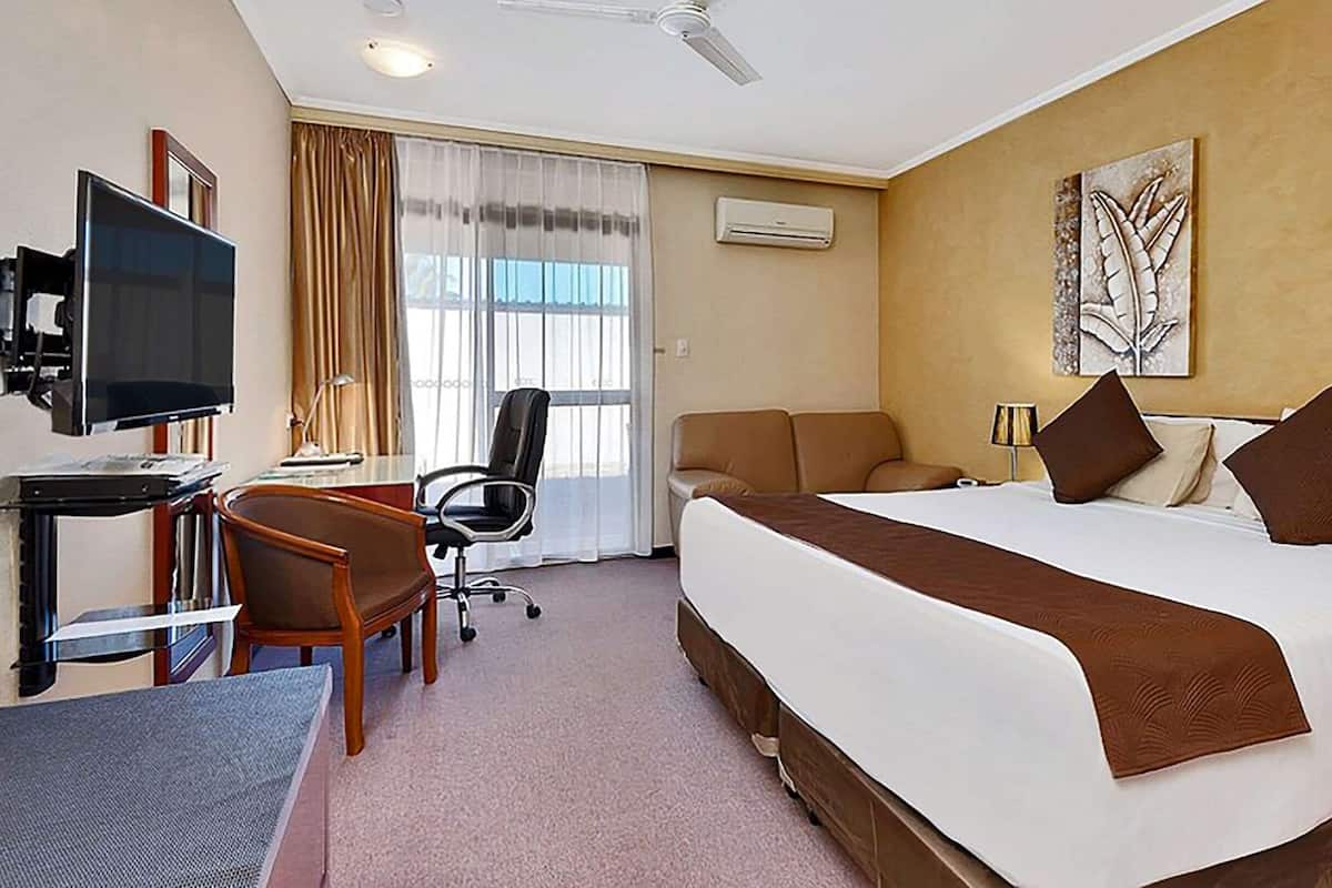 Ein Hotelzimmer mit einem Bett, einem Schreibtisch mit Computer, einem Sessel, einem Fernseher und einem Fenster mit Vorhängen.