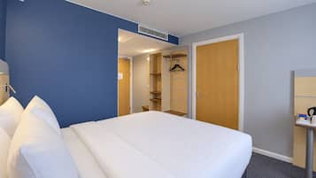 Ett hotellrum med en stor säng, en garderob, en spegel och ett skrivbord med en vattenkokare.