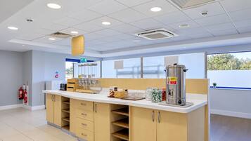 A clean, modern kitchenette with a white countertop, wooden cabinets, and a stainless steel coffee maker.