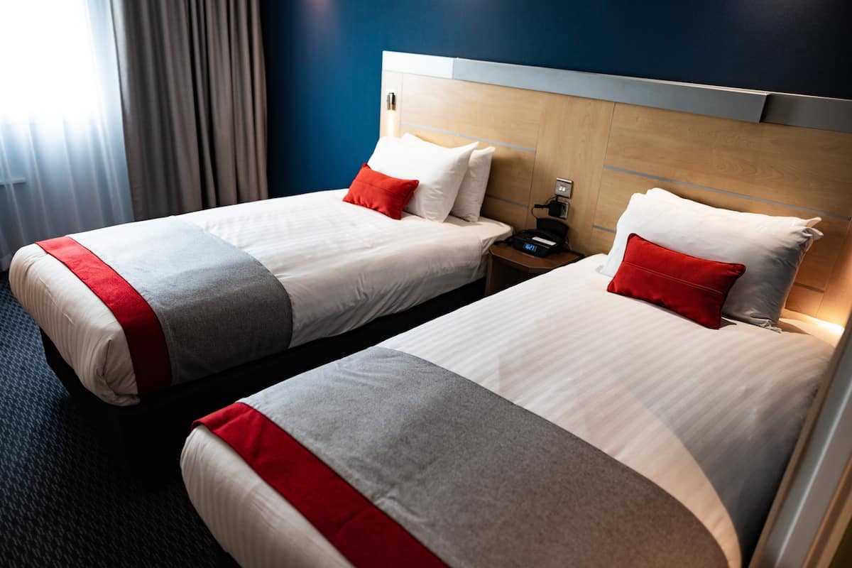 Two single beds with red and grey bedding, wooden headboards, and bedside tables with lamps.
