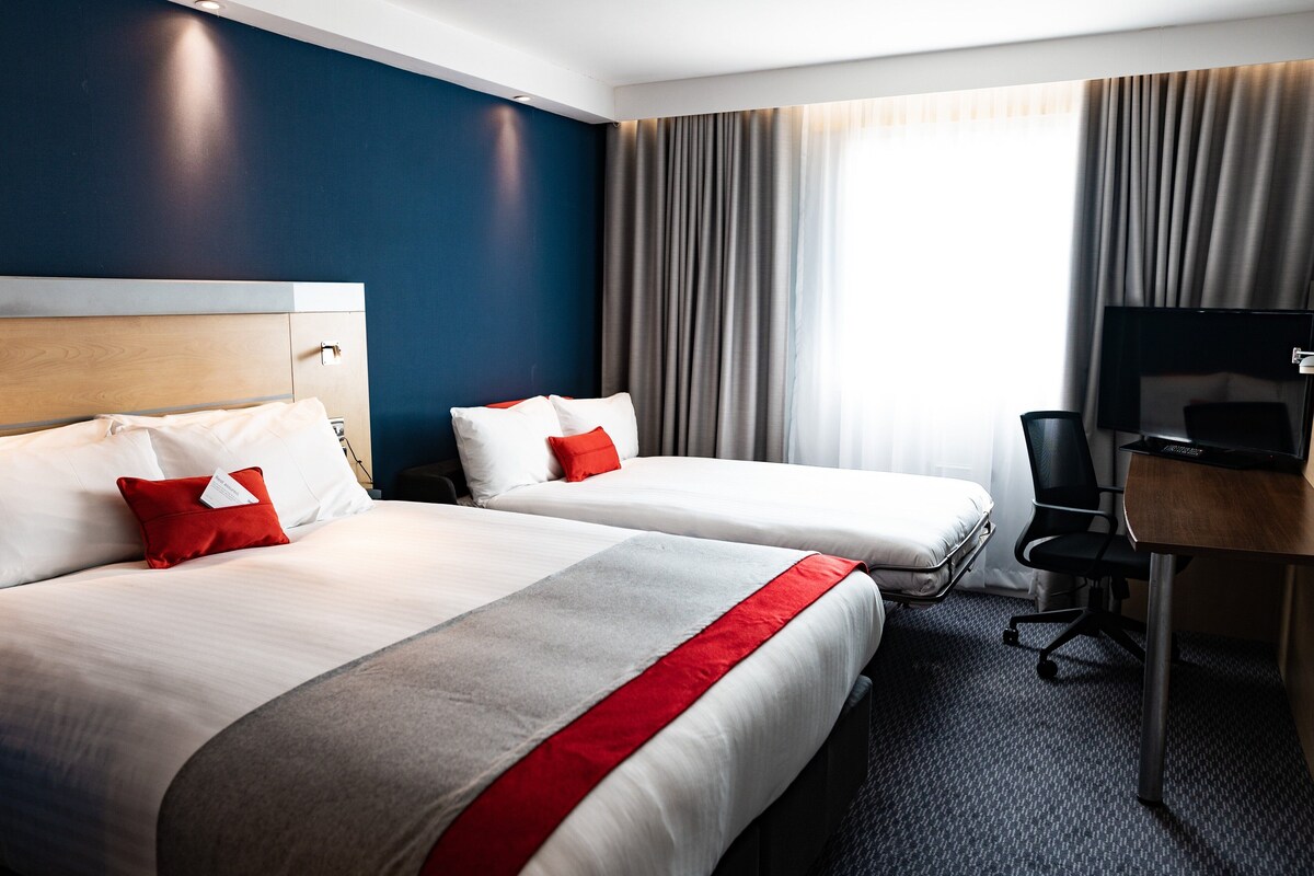 Ett hotellrum med två sängar, ett skrivbord, en stol och en tv.