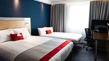 Quarto de hotel com duas camas, uma escrivaninha, uma cadeira e uma televisão.