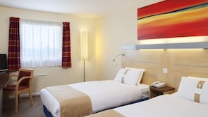 Une chambre d’hôtel avec deux lits, un bureau, une chaise, une lampe et un tableau au mur.