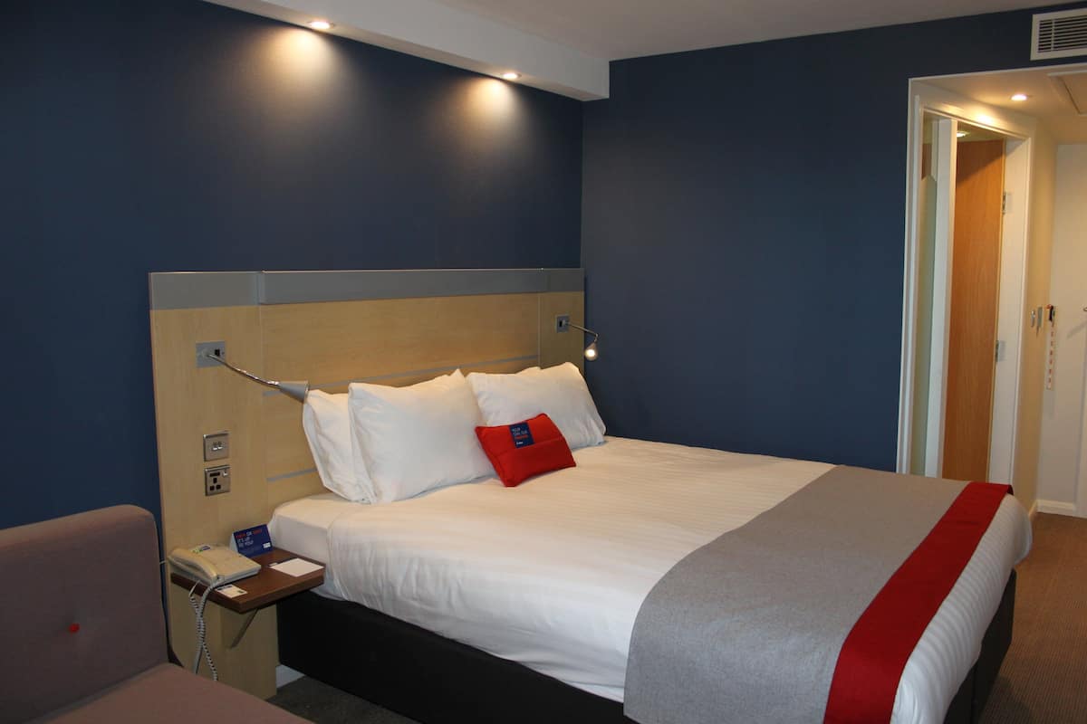 A hotel room with a large bed, a bedside table with a phone, and a red pillow.