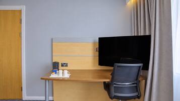 Una habitación de hotel con escritorio, una silla, televisor y puerta.