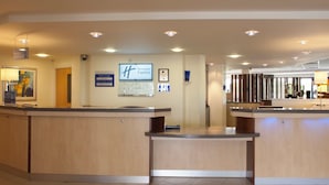 Un espace d’accueil d’hôtel avec un comptoir de réception en bois, une horloge et un panneau indiquant « Holiday Inn Express ».