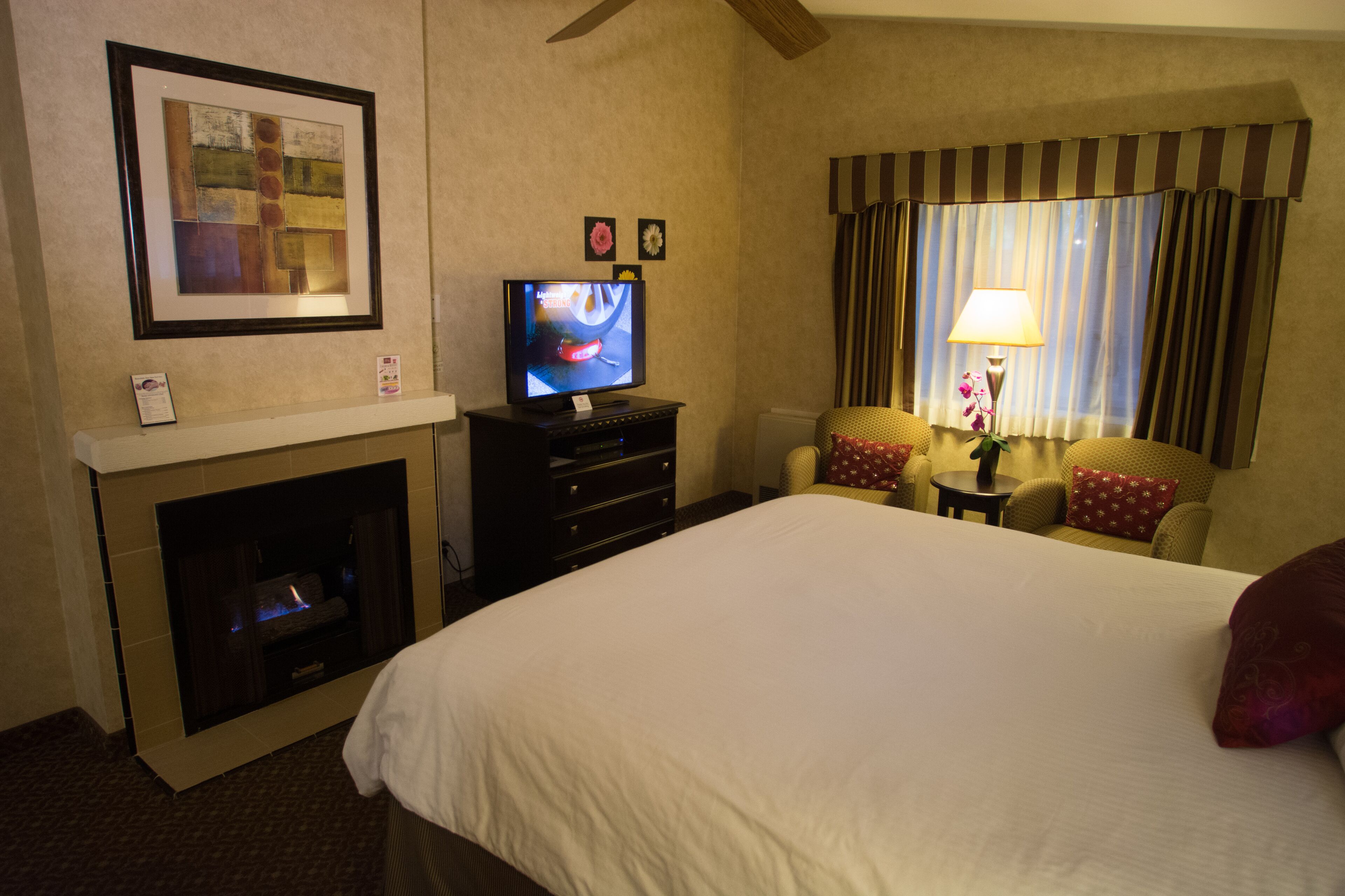 Habitación de hotel con una cama grande, televisión, chimenea, sofá y ventana con cortinas.