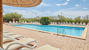 Une piscine entourée de verdure, avec des chaises longues et des parasols.