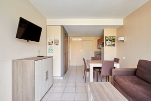 A modern apartment with a kitchenette, a dining area, a living room with a sofa, and a TV mounted on the wall. - Résidence Odalys Du Golfe (Agde)