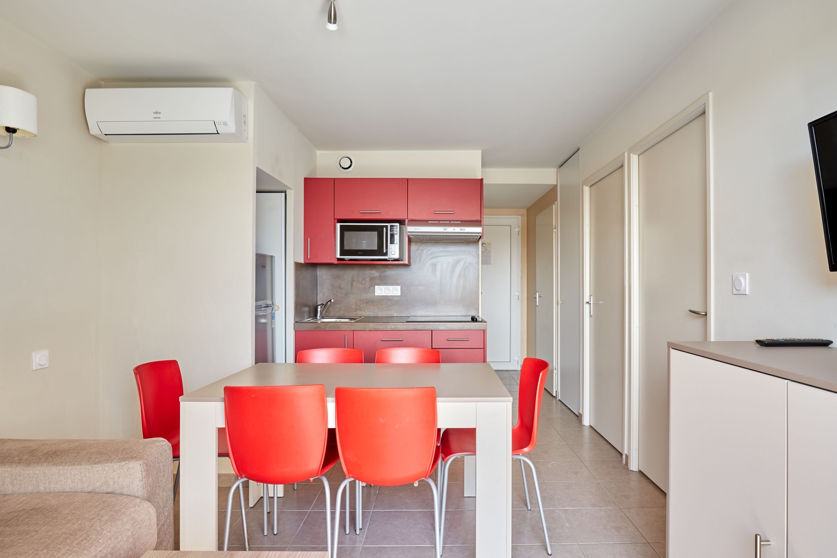 Een moderne keuken met rode kastjes, een magnetron en een spoelbak. Er staat een eettafel met vier rode stoelen.