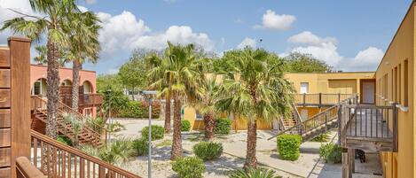 A courtyard with palm trees, a wooden staircase, and a yellow building.