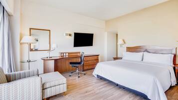 A hotel room with a large bed, a desk with a chair, a television, and a mirror.