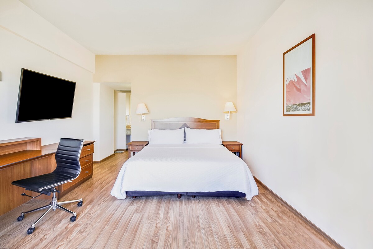 Hotelkamer met een bed, een bureau met stoel, een flatscreen-tv, twee bedlampen en een ingelijst kunstwerk aan de muur.