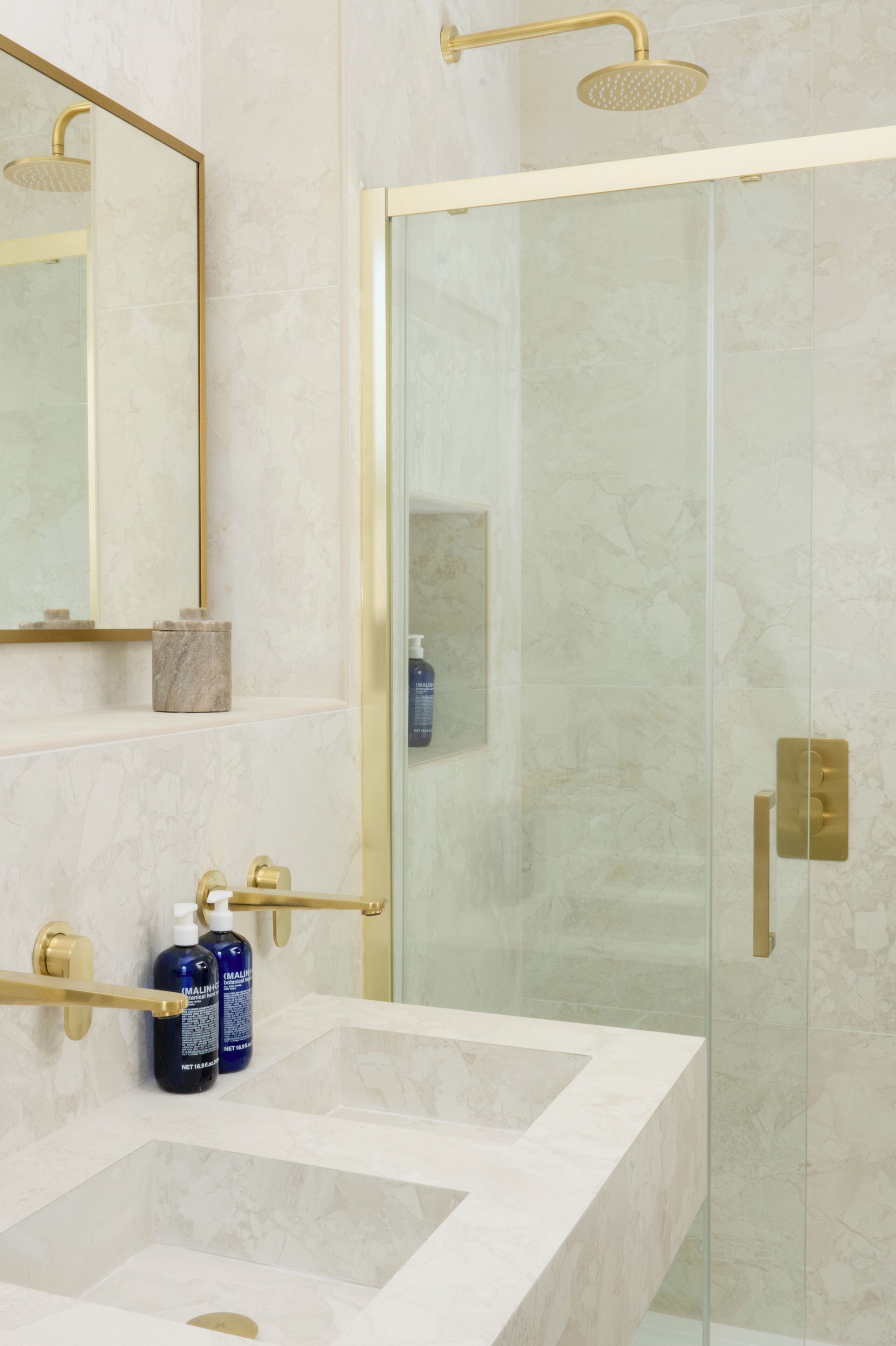 A bathroom with a glass-enclosed shower, a white marble sink, and a gold-framed mirror.
