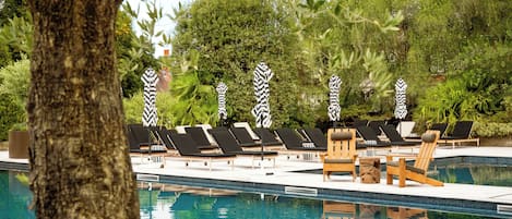 A pool area with lounge chairs and umbrellas, surrounded by trees and greenery.