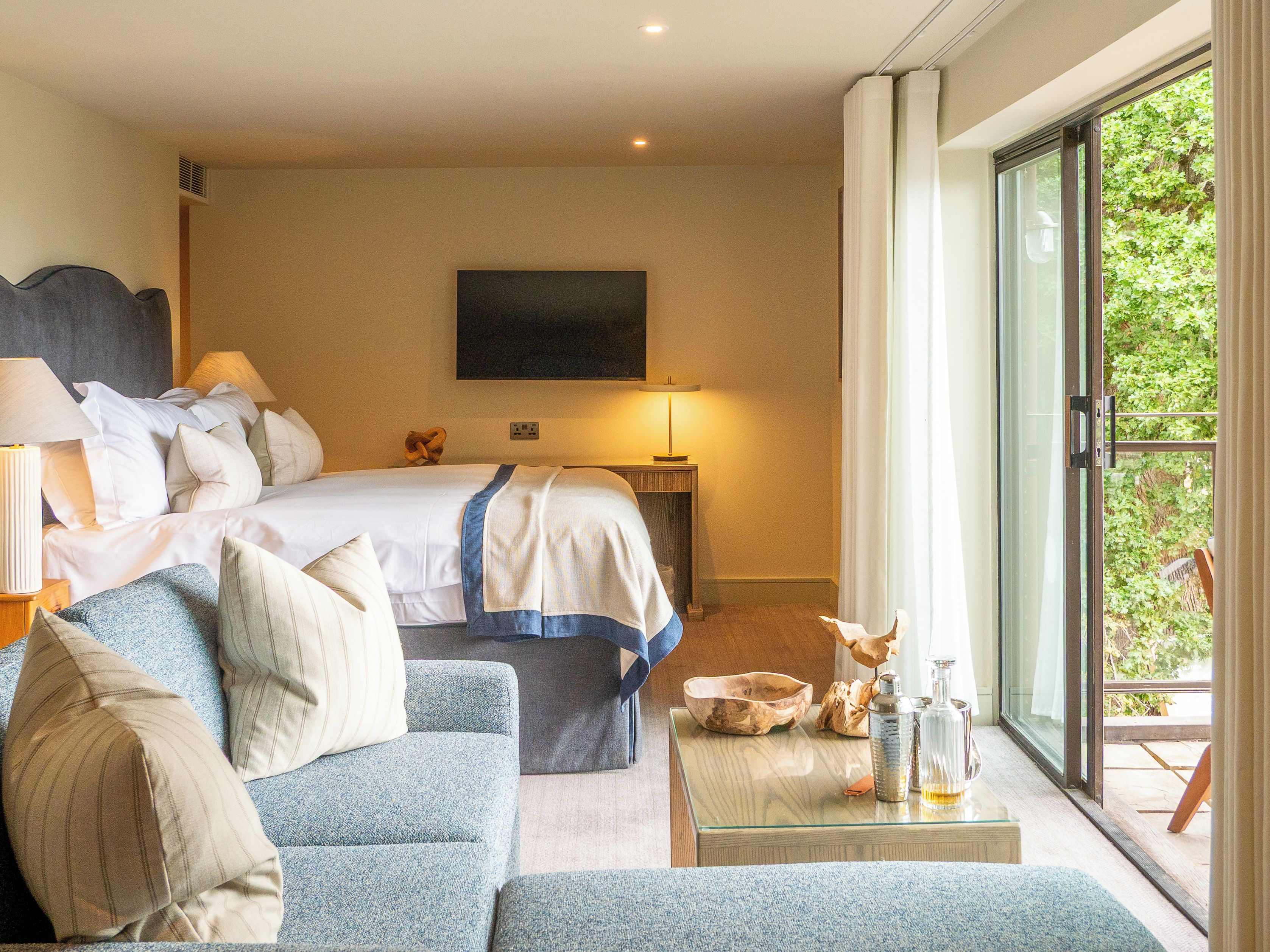 Ein Hotelzimmer mit Bett, Sofa, Tisch mit Flasche und Glas, Fernseher an der Wand und einer Glastür zum Außenbereich.