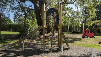 Explore the park's playground, featuring a climbing structure, swing set, and play area surrounded by trees and a hedge.