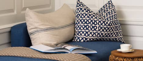 A room with a blue sofa, a patterned pillow, a book, and a small round table with a cup and saucer.