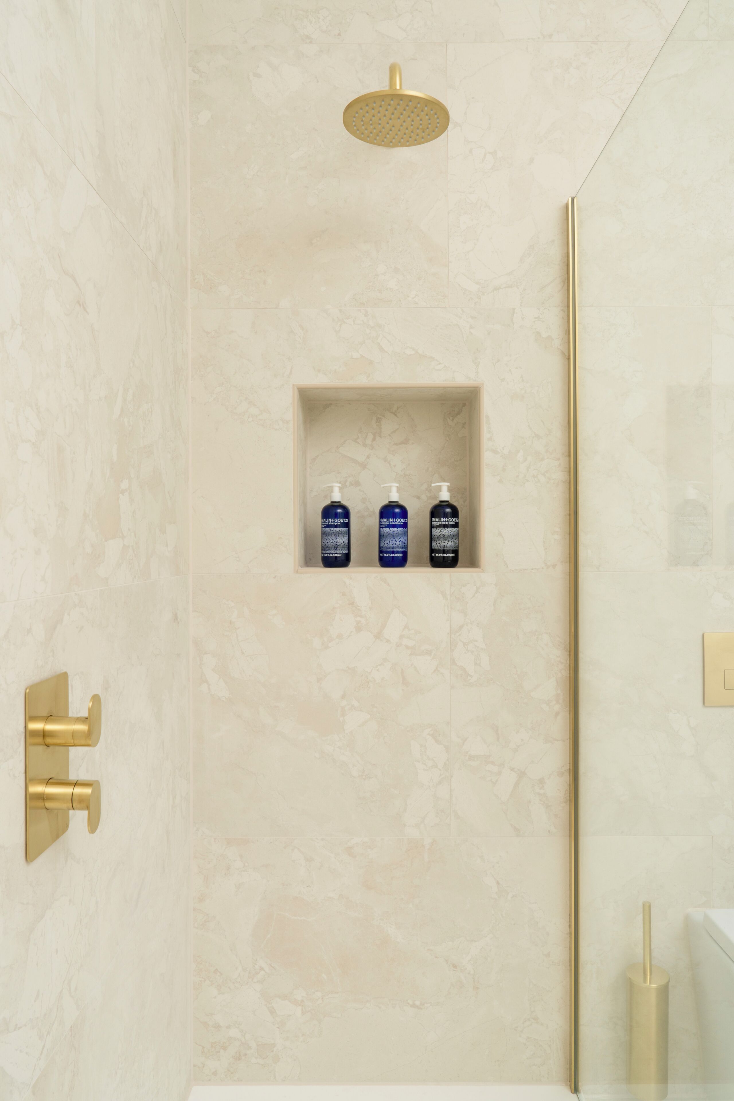 Ein Badezimmer mit Dusche, Waschtisch und Ablagefläche mit drei Shampoo-Flaschen.