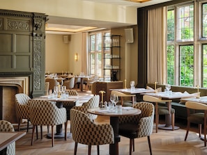A restaurant with checkered chairs, tables set with glasses, and a fireplace. - The NICI New Forest (Lymington)