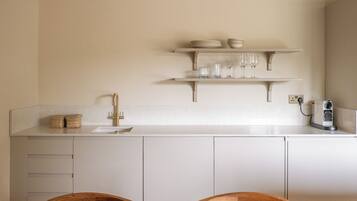 Una cocina moderna con encimera blanca, grifo dorado y comedor con mesa y sillas de madera.