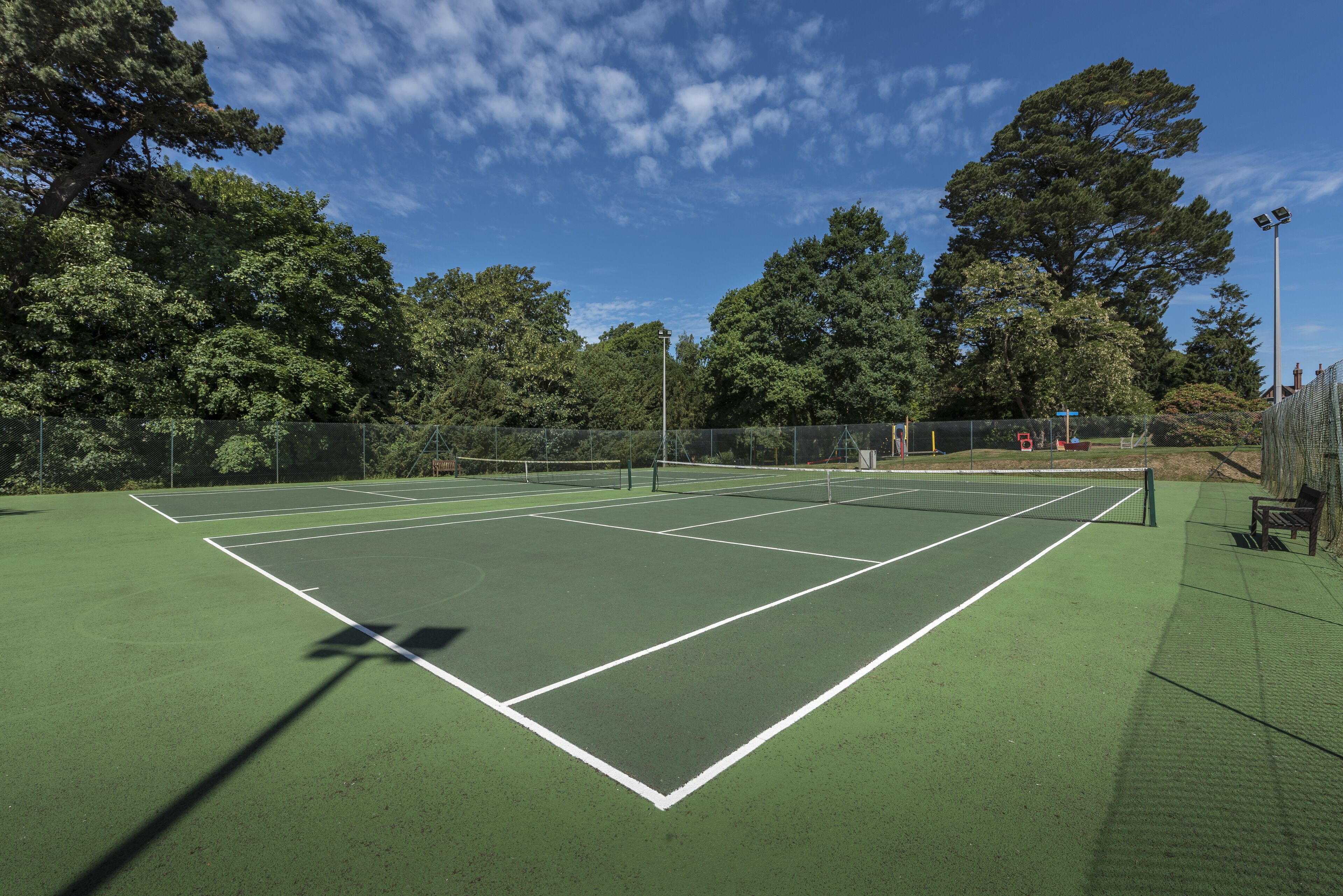Een tennisbaan met een net, omgeven door bomen en een hek.