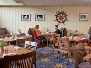 Enjoy meals in a nautical-themed dining area with wooden tables, potted plants, and a striking ship's wheel.