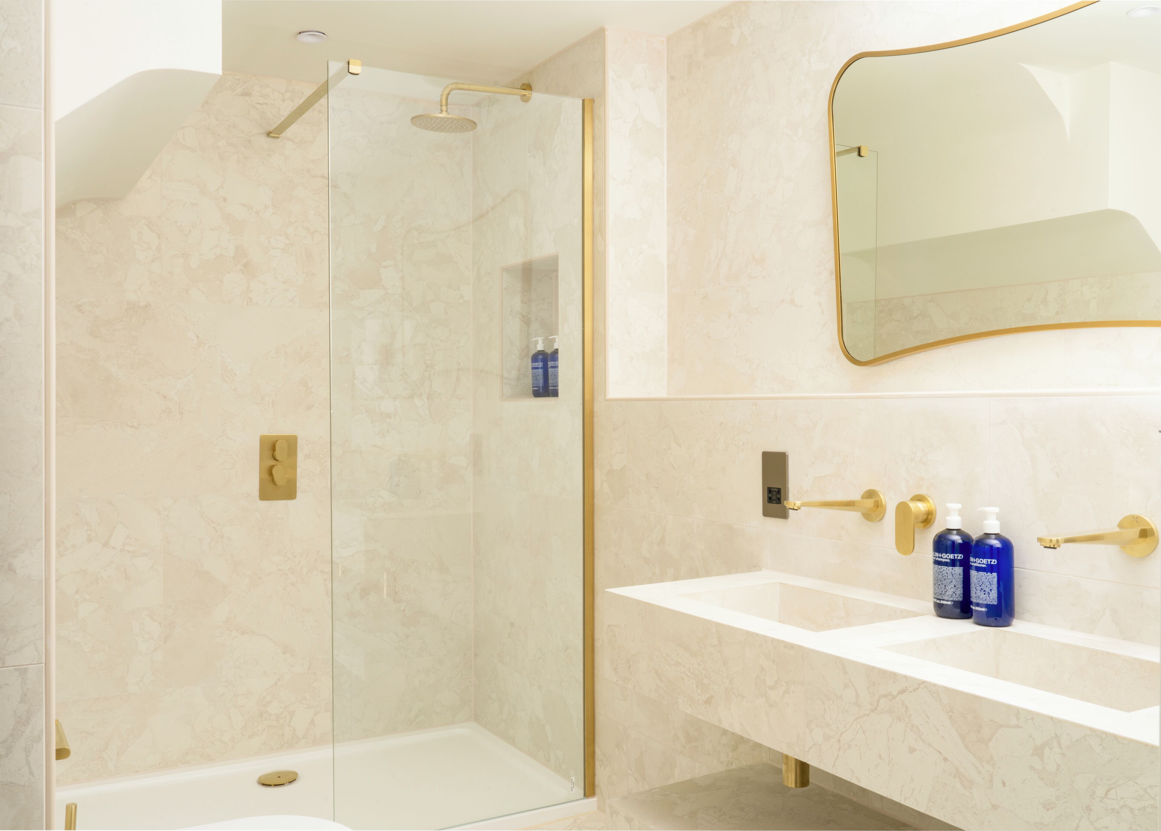 Une salle de bain moderne avec une douche à parois de verre, un meuble-lavabo blanc doté de robinetterie dorée et un grand miroir.