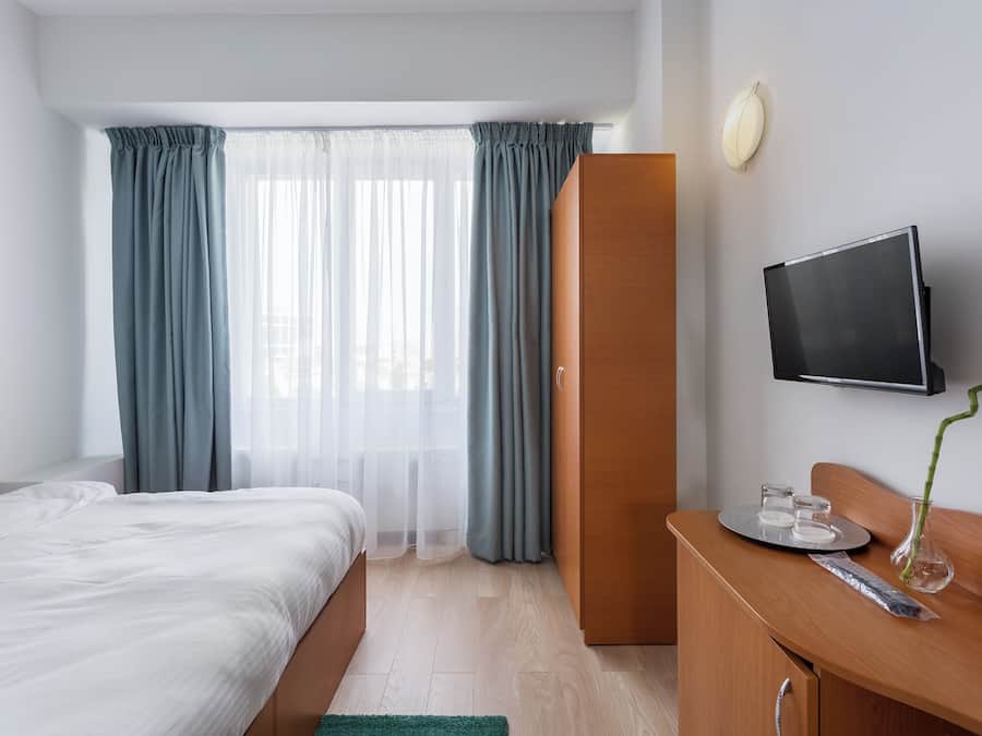 A hotel room with a bed, a desk, a television, and a window with curtains.