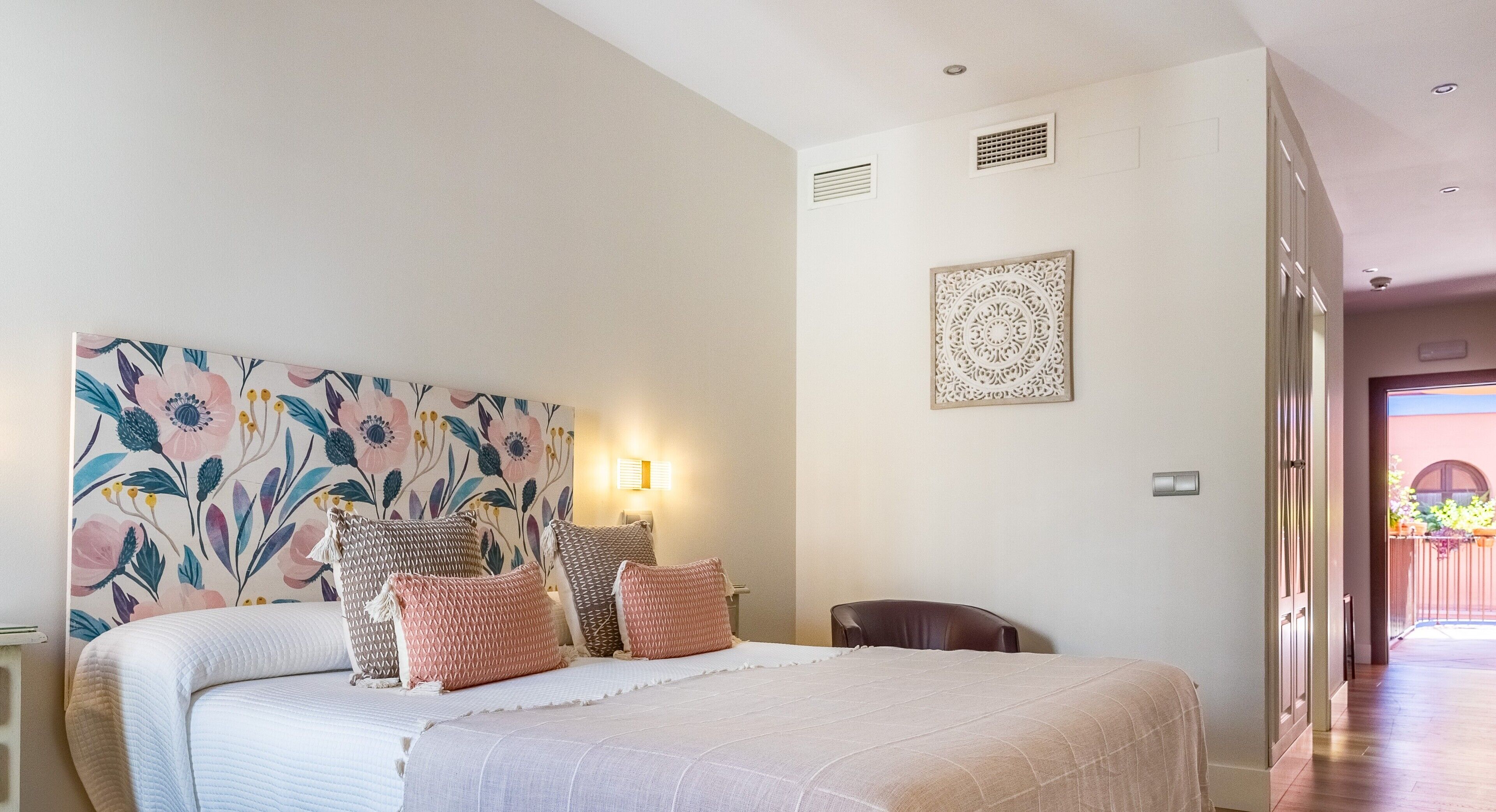A bedroom with a large bed, a floral headboard, a wall-mounted light, and a decorative wall piece.