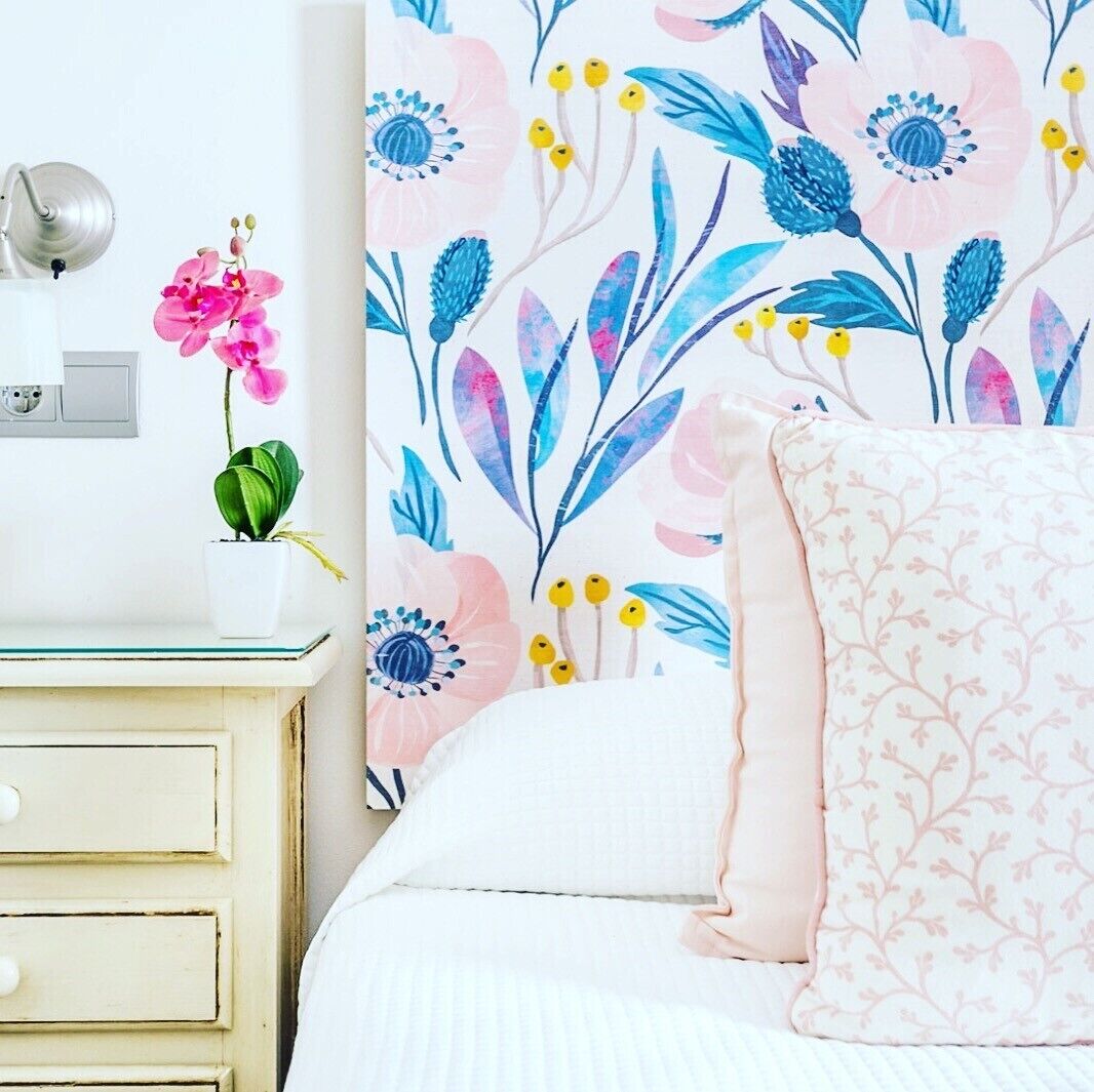 Een slaapkamer met een bed, nachtkastje, lamp en een bloemen behang muur.