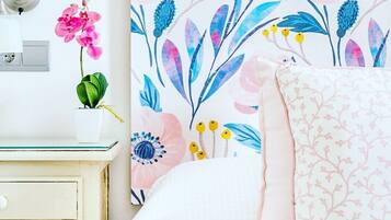 Een slaapkamer met een bed, nachtkastje, lamp en een bloemen behang muur.