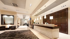 Un moderno vestíbulo de hotel con una recepción, zona de estar y un espejo grande.