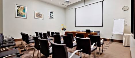 Une salle de conférence équipée d’un tableau blanc, d’un écran de projection et de plusieurs chaises disposées autour d’une table.