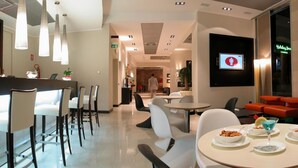 Un moderno vestíbulo de hotel con una mesa de recepción, zonas de estar y una pantalla de televisión que muestra un círculo rojo con una figura blanca.