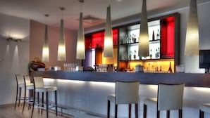 Un área de bar moderna con una barra alargada, taburetes y una variedad de botellas y vasos.